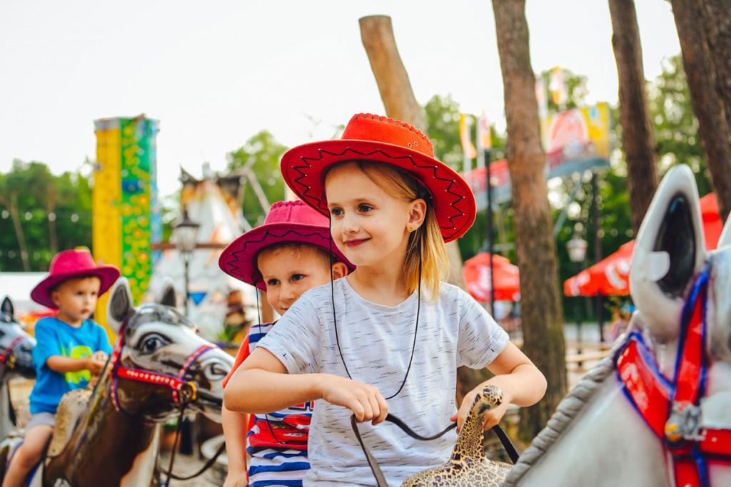 Zadowolone dzieci w kowbojskich kapeluszach na zabawkowych koniach